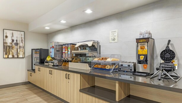A modern kitchen area with a self-serve station, including a waffle maker, coffee machine, and various food items.