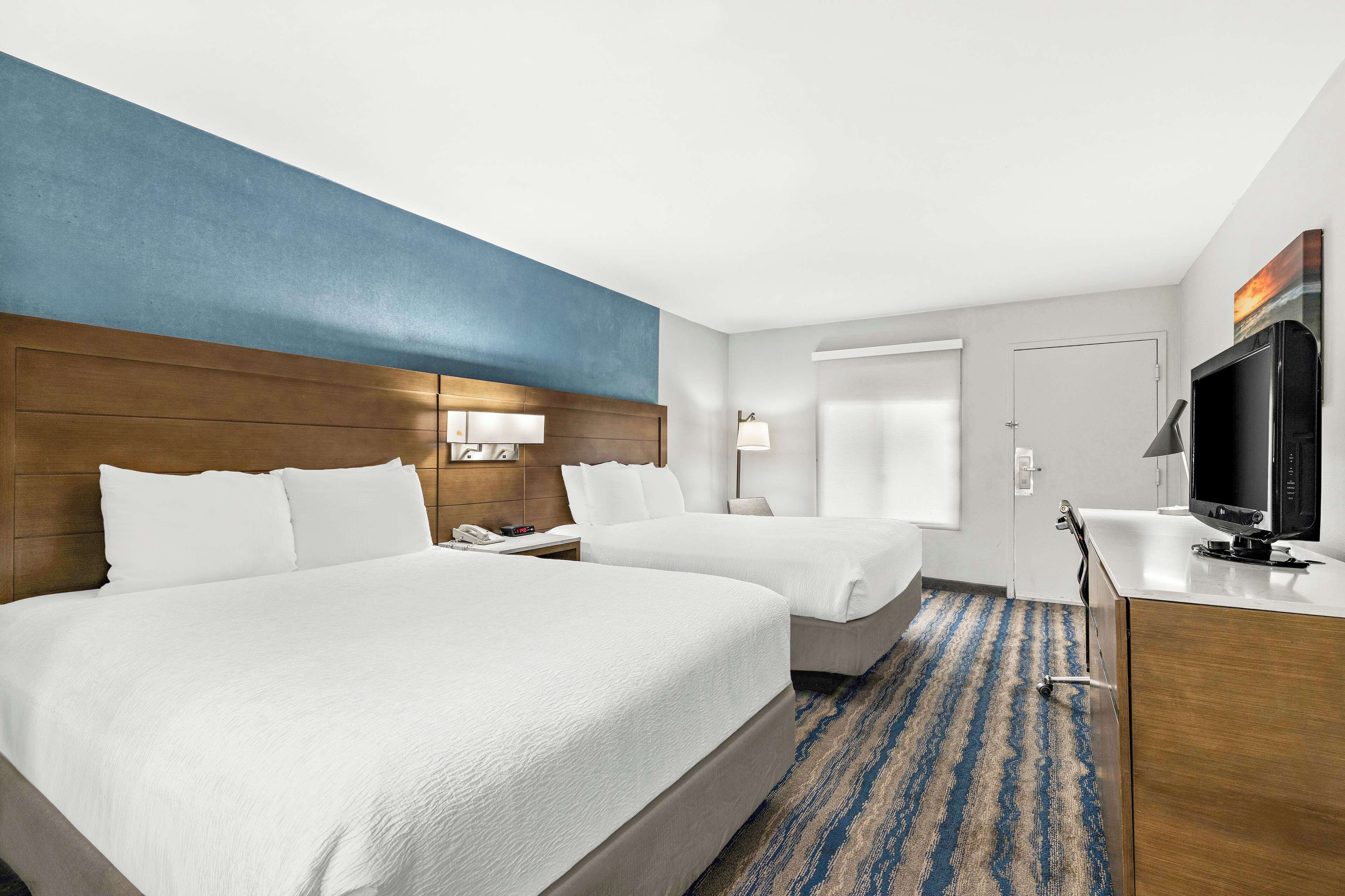 Habitación de hotel con dos camas, televisión, escritorio y puerta al baño.