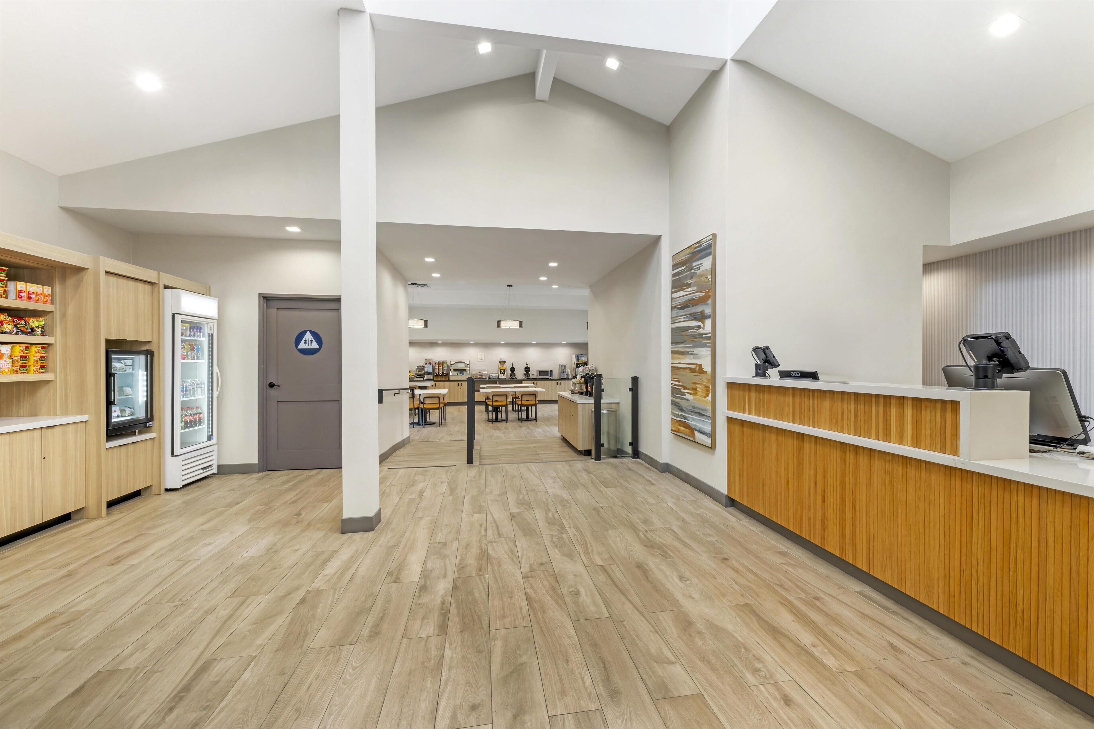 A spacious lobby with a wooden reception desk, a refrigerator, and a vending machine.