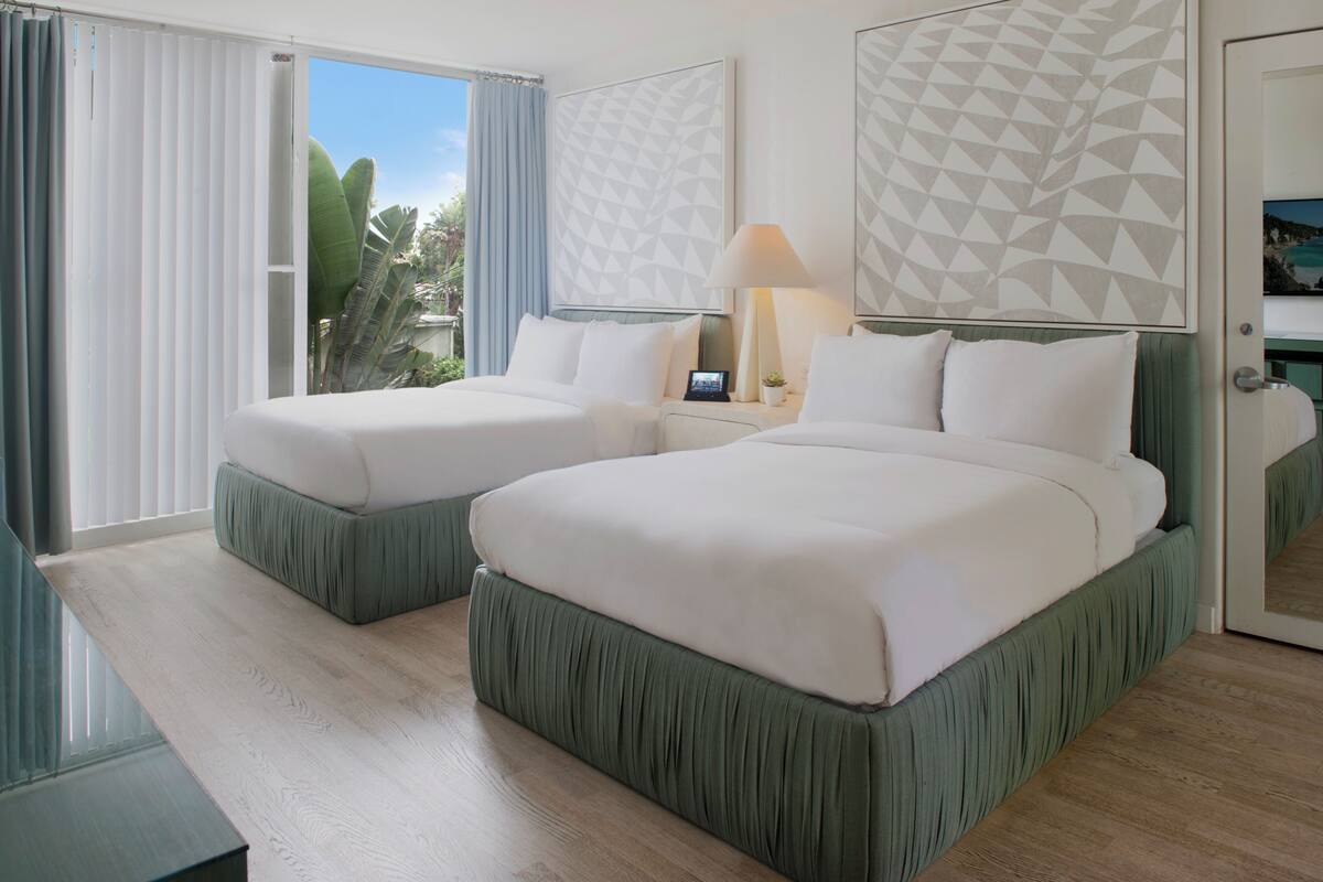 Habitación de hotel con dos camas, un ventanal con cortinas, una lámpara y un diseño geométrico en la pared.