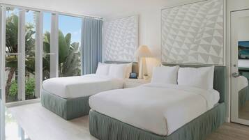 A hotel room with two beds, a large window with curtains, a lamp, and a geometric wall design.