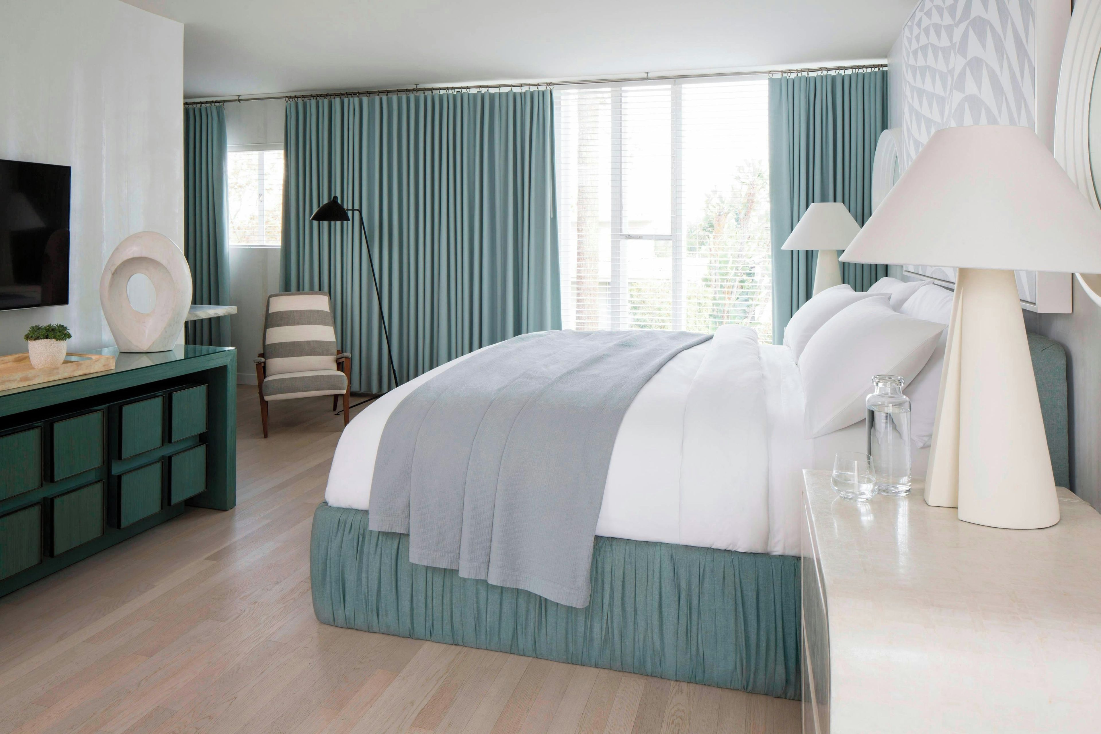 A modern bedroom with a large bed, a desk, a chair, and a TV.