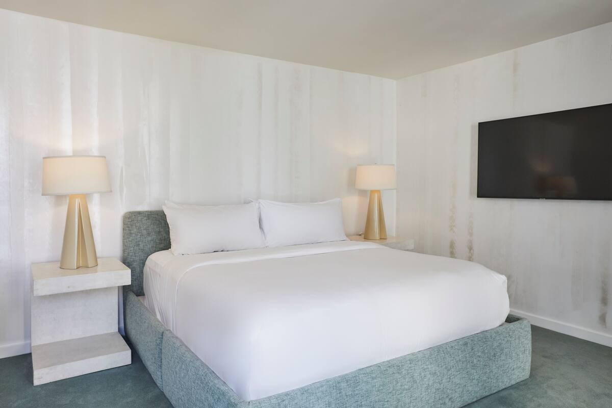 Un dormitorio ordenado con una cama, dos mesitas de noche y un televisor de pantalla plana montado en la pared.