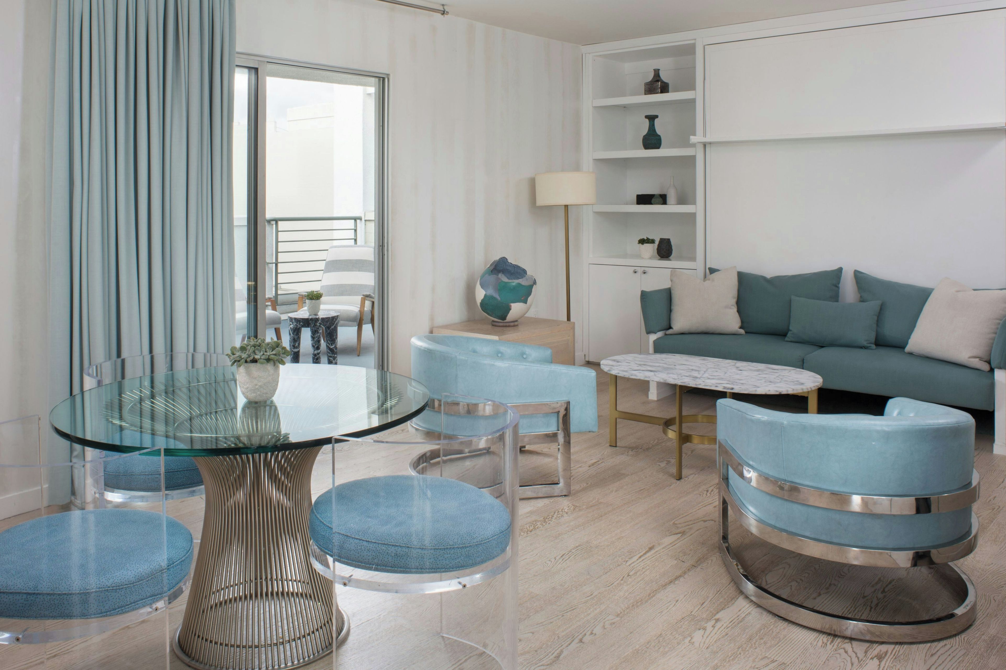 Una sala moderna con una mesa de vidrio, sillas tapizadas en azul, un sofá y una estantería.