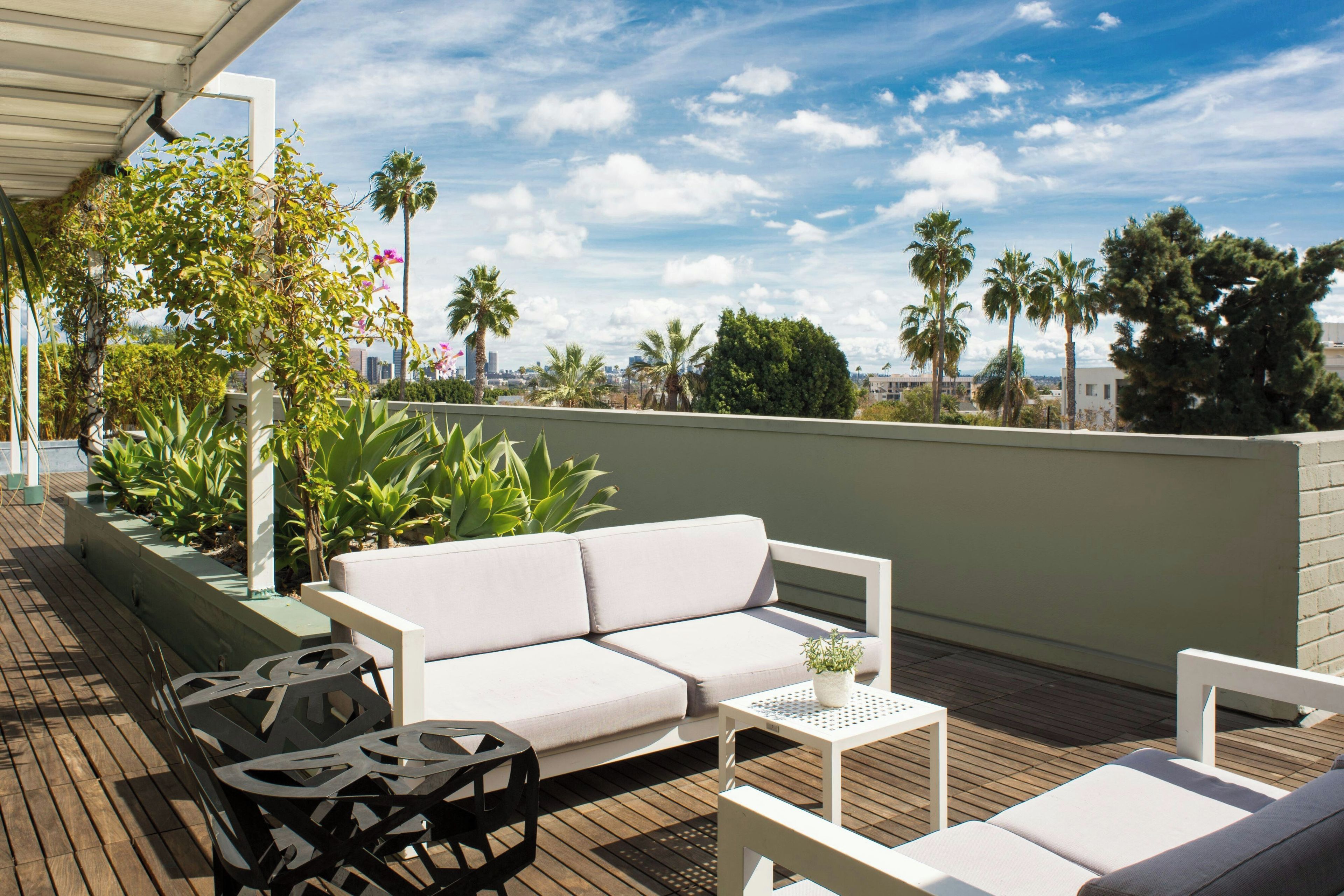 Terraço no telhado com um sofá branco, uma mesa de metal e uma poltrona estofada.
