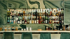 Un bar con una pared de mármol y varias botellas de licor. Hay cuatro taburetes de bar frente al mostrador.