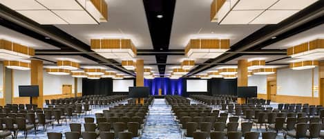 A conference room with rows of chairs, a large screen, and a blue curtain backdrop.