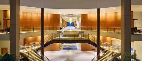 A multi-level atrium with a central staircase, wooden panel walls, and a glass ceiling.