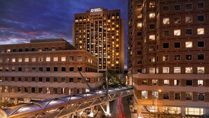 Um hotel com vários andares, com um letreiro grande 'Hyatt Regency', uma passarela e uma rua urbana bem iluminada à noite.