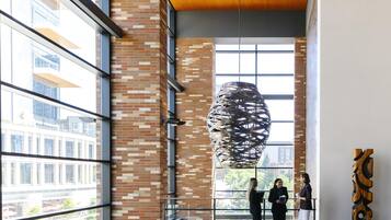A modern interior with a hanging sculpture, brick walls, large windows, and a blue patterned carpet.