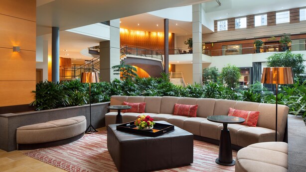 Um hall amplo com um sofá curvo, uma mesa de centro com uma bandeja de flores, um tapete estampado e uma escadaria para um andar superior.