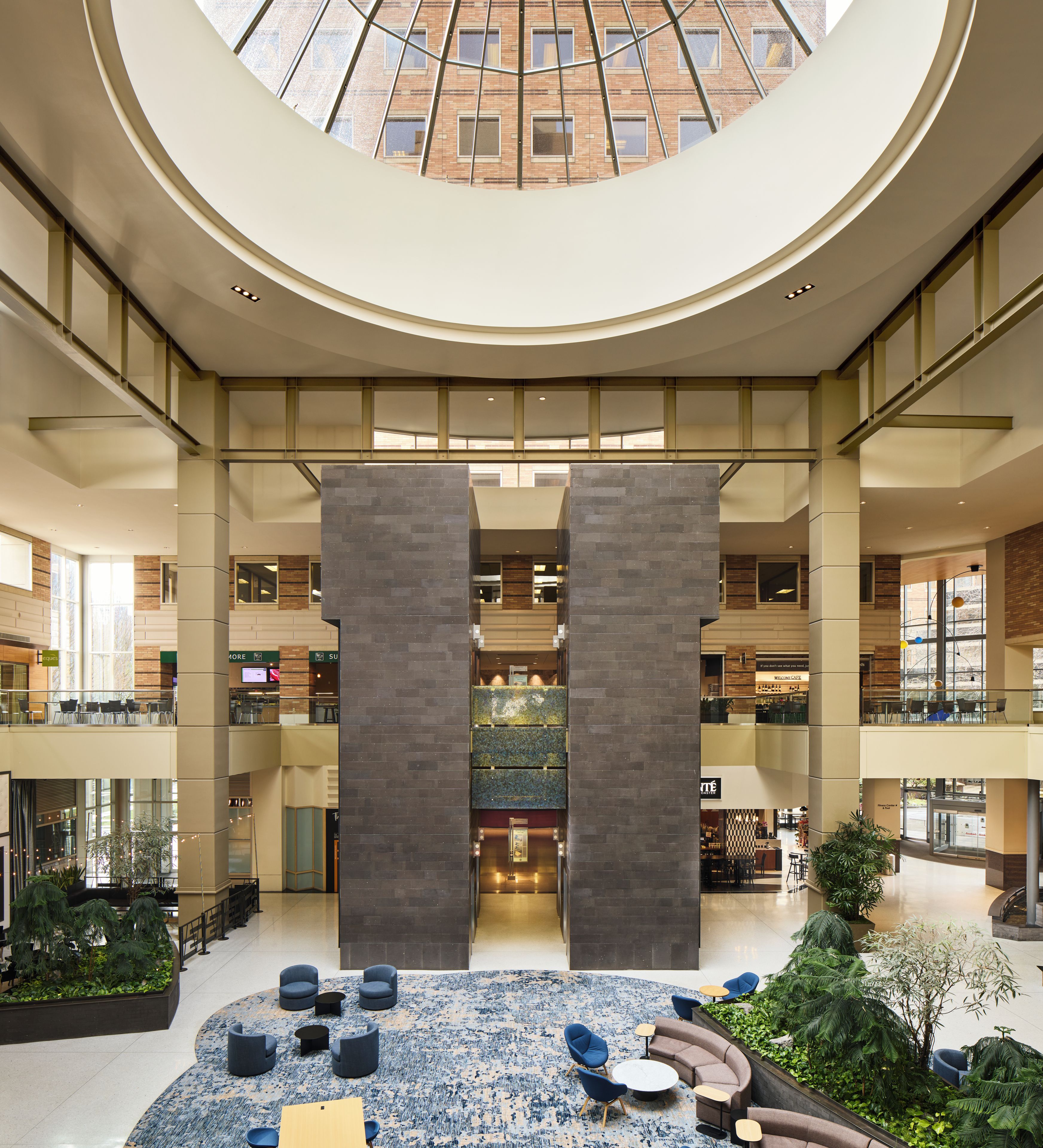 A spacious atrium with a central column, multiple levels, and seating areas with plants.
