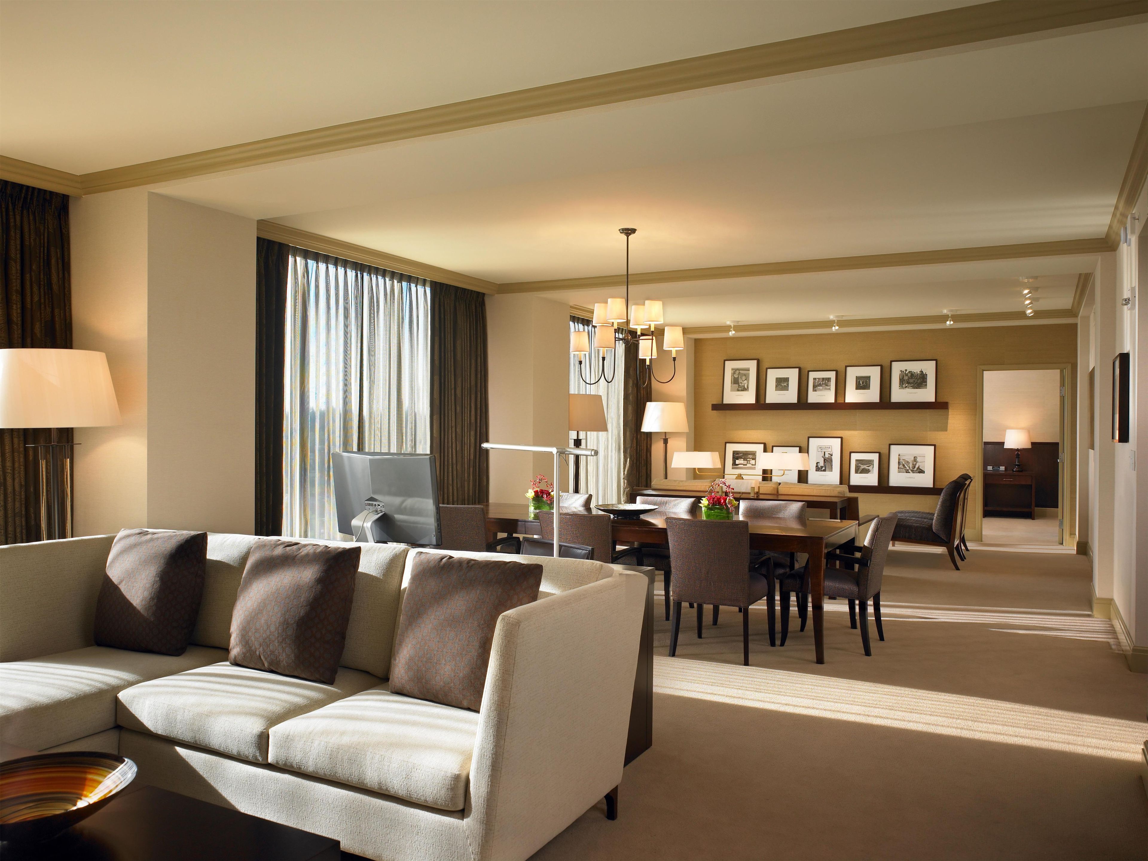 A hotel room with a sofa, dining table, chairs, and a desk with a computer.