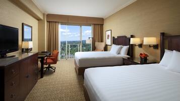 Quarto de hotel com duas camas, uma escrivaninha, televisão e vista para o exterior.