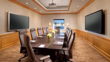A conference room with a long table, multiple chairs, a projector, and a large screen.