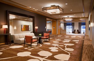 A hotel lobby with a sofa, chairs, a table, and a carpet with a floral pattern.