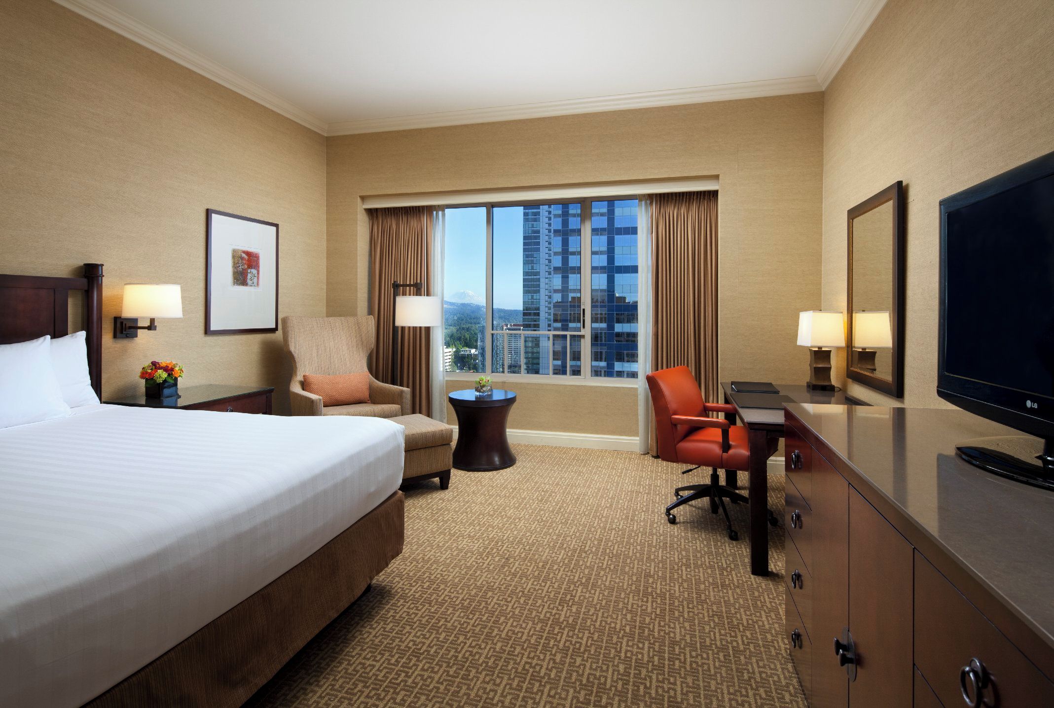 Habitación de hotel con una cama grande, un escritorio con silla, televisión y ventana con vista a la ciudad.