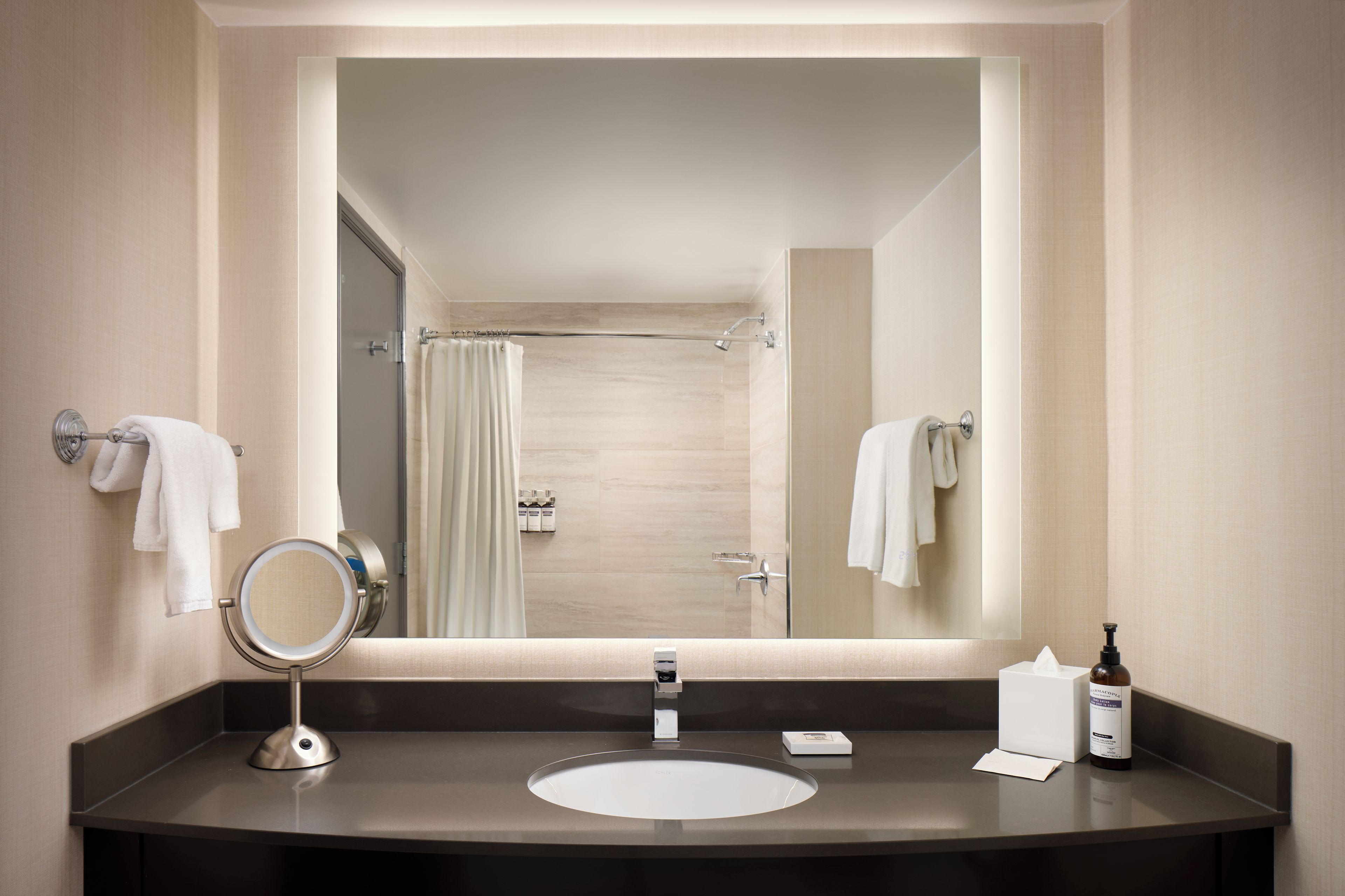A modern bathroom with a large mirror, a round mirror, a sink, and a shower area.