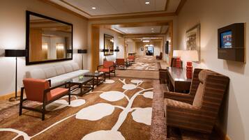 A hotel lobby with a sofa, chairs, a coffee table, a carpet with a leaf pattern, and a television screen.