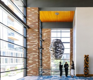 Un interior moderno con una escultura colgante, paredes de ladrillo, ventanas amplias y una alfombra azul estampada.
