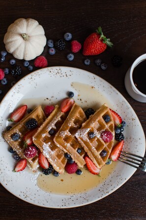 Waffles served with fresh berries and maple syrup on a table.