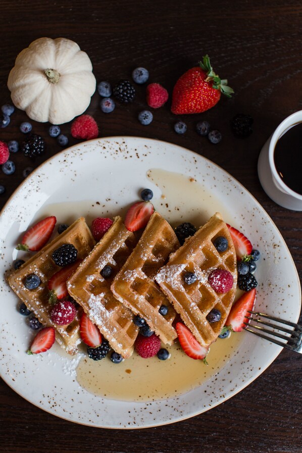 A plate of waffles with strawberries and blueberries, a small pumpkin, and a cup of coffee on a wooden table. - Hyatt Regency Bellevue (Bellevue)