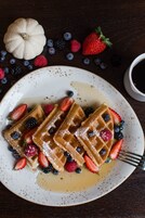 A plate of waffles with strawberries and blueberries, a small pumpkin, and a cup of coffee on a wooden table.
