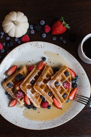 Waffles served with fresh berries and maple syrup on a table.