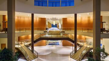 A multi-level atrium with a central staircase, wooden panel walls, and a glass ceiling.