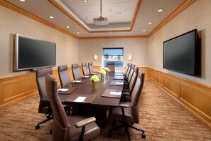 Un salón de conferencias con una larga mesa, varias sillas, un proyector y una pantalla grande.