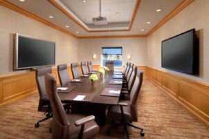 Uma sala de conferências com uma mesa comprida, várias cadeiras, um projetor e uma tela grande.