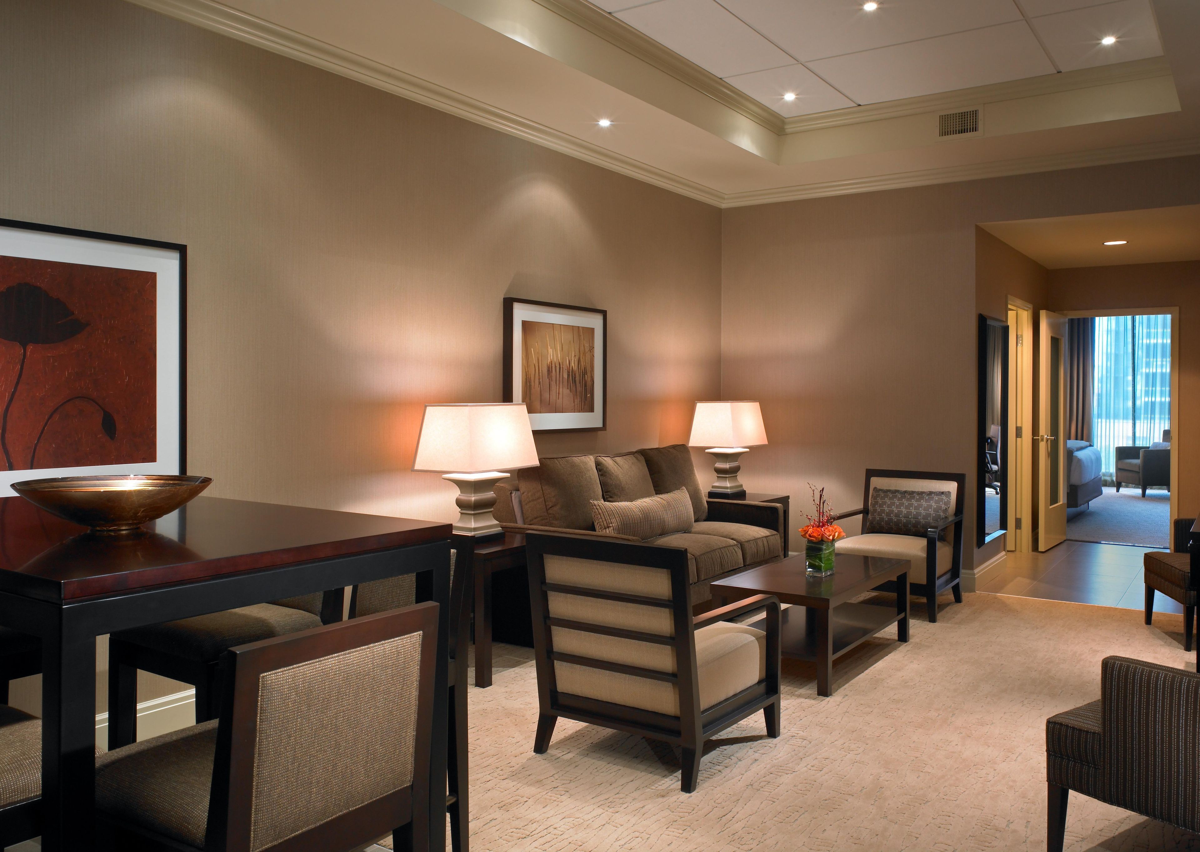 A hotel room with a sofa, armchairs, a coffee table, a dining table, and a painting on the wall.