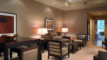 Habitación de hotel con sofá, sillones, una mesa de centro, una mesa de comedor y un cuadro en la pared.