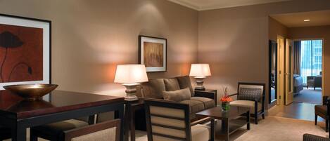 A hotel room with a sofa, armchairs, a coffee table, a dining table, and a painting on the wall.