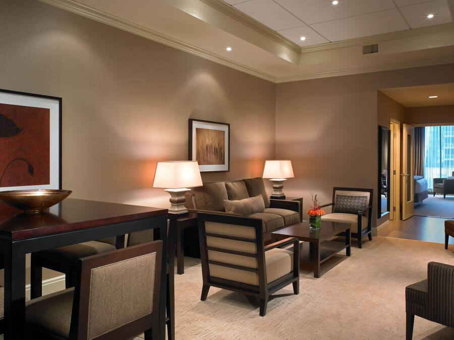 Habitación de hotel con sofá, sillones, una mesa de centro, una mesa de comedor y un cuadro en la pared.