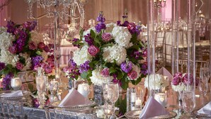 Mesa de jantar formal com taças de cristal, talheres e arranjos florais elegantes.