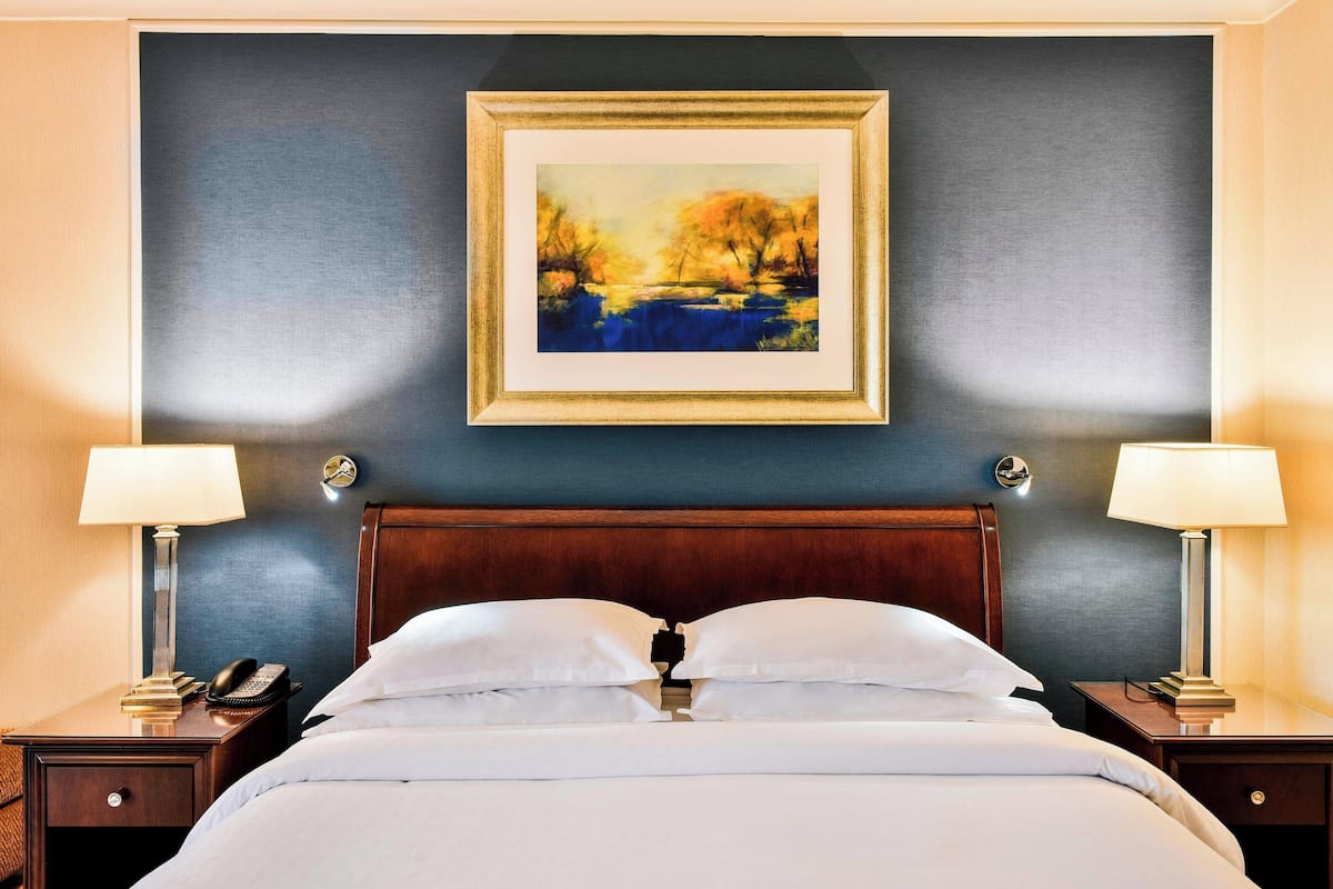 Une chambre d’hôtel avec un grand lit, deux tables de chevet avec des lampes, un tableau au mur et un téléphone sur l’une des tables.