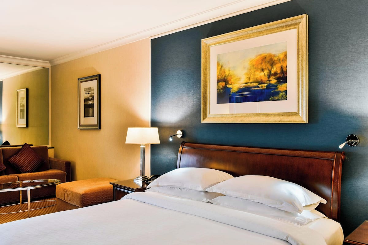 Une chambre d’hôtel avec un lit, une table de chevet, une lampe, un tableau encadré au mur et un canapé.
