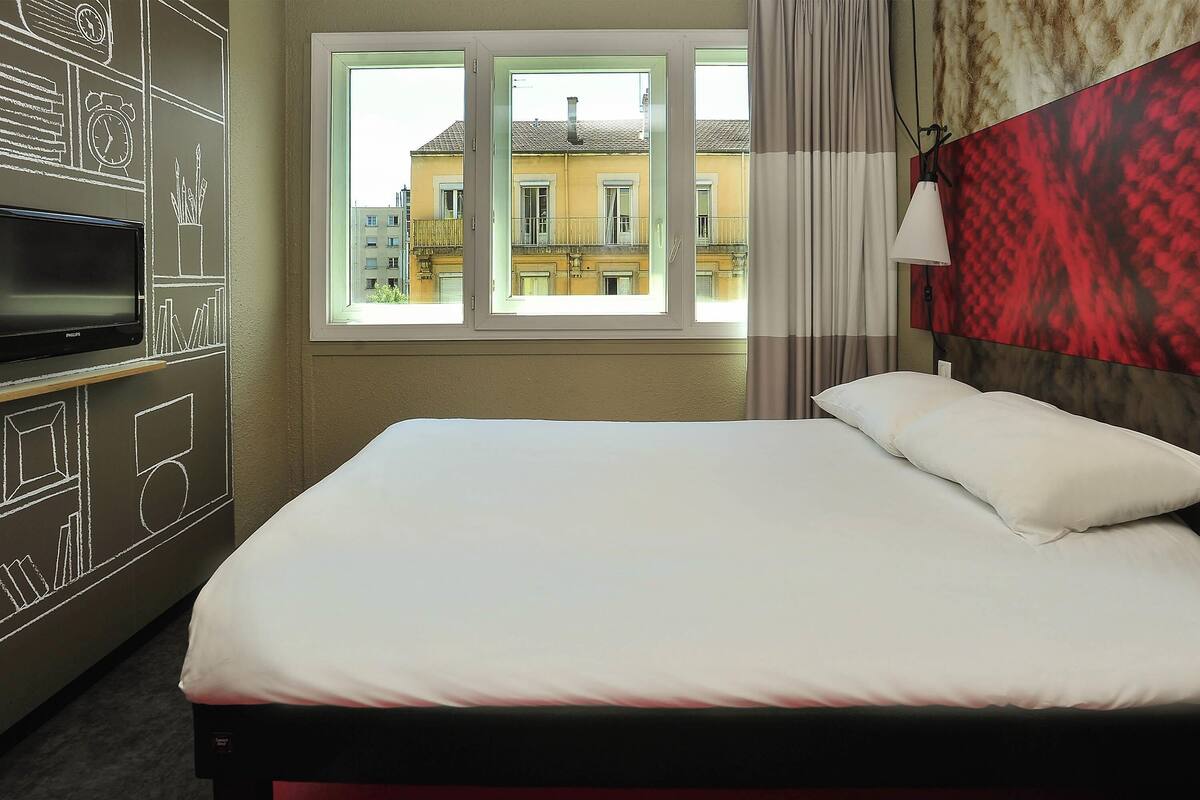 Een hotelkamer met een bed, een televisie en een raam met uitzicht op gebouwen.