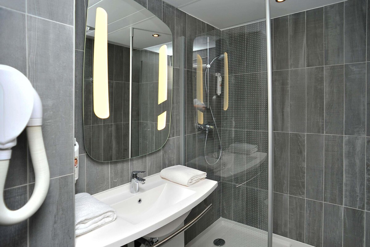 A modern bathroom with a white sink, mirror, and shower.