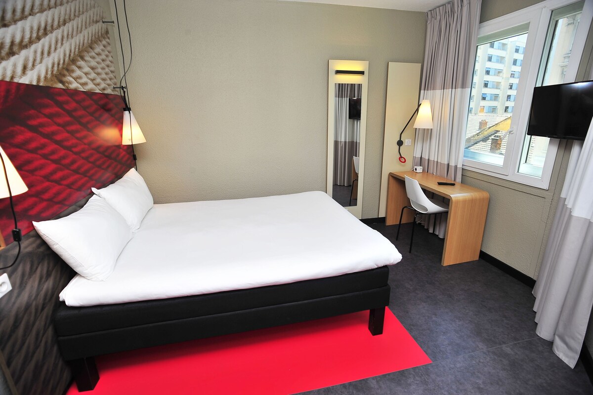 A hotel room with a bed, desk, chair, and a TV.