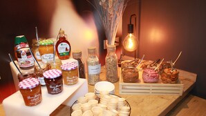 Diversos alimentos y condimentos sobre una mesa de madera, incluyendo frascos de miel, mermeladas y salsas, con una bombilla de luz al fondo.
