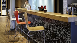A bar area with a reception desk, bar stools, and a wall with abstract designs. - Ibis Lyon Centre (Lyon)