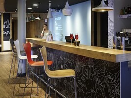 Zona de bar con mostrador de recepción, taburetes y una pared con diseños abstractos.