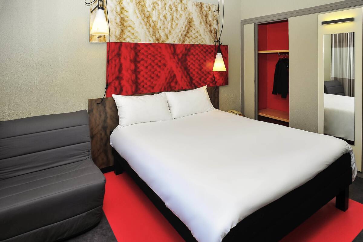 Een moderne hotelkamer met een groot bed, een sofa, een rood tapijt en een inloopkast met spiegel.