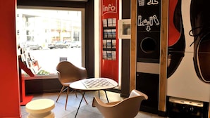 A modern interior with a red wall, a table with chairs, a guitar, and a poster with recycling symbols. - Ibis Lyon Centre (Lyon)