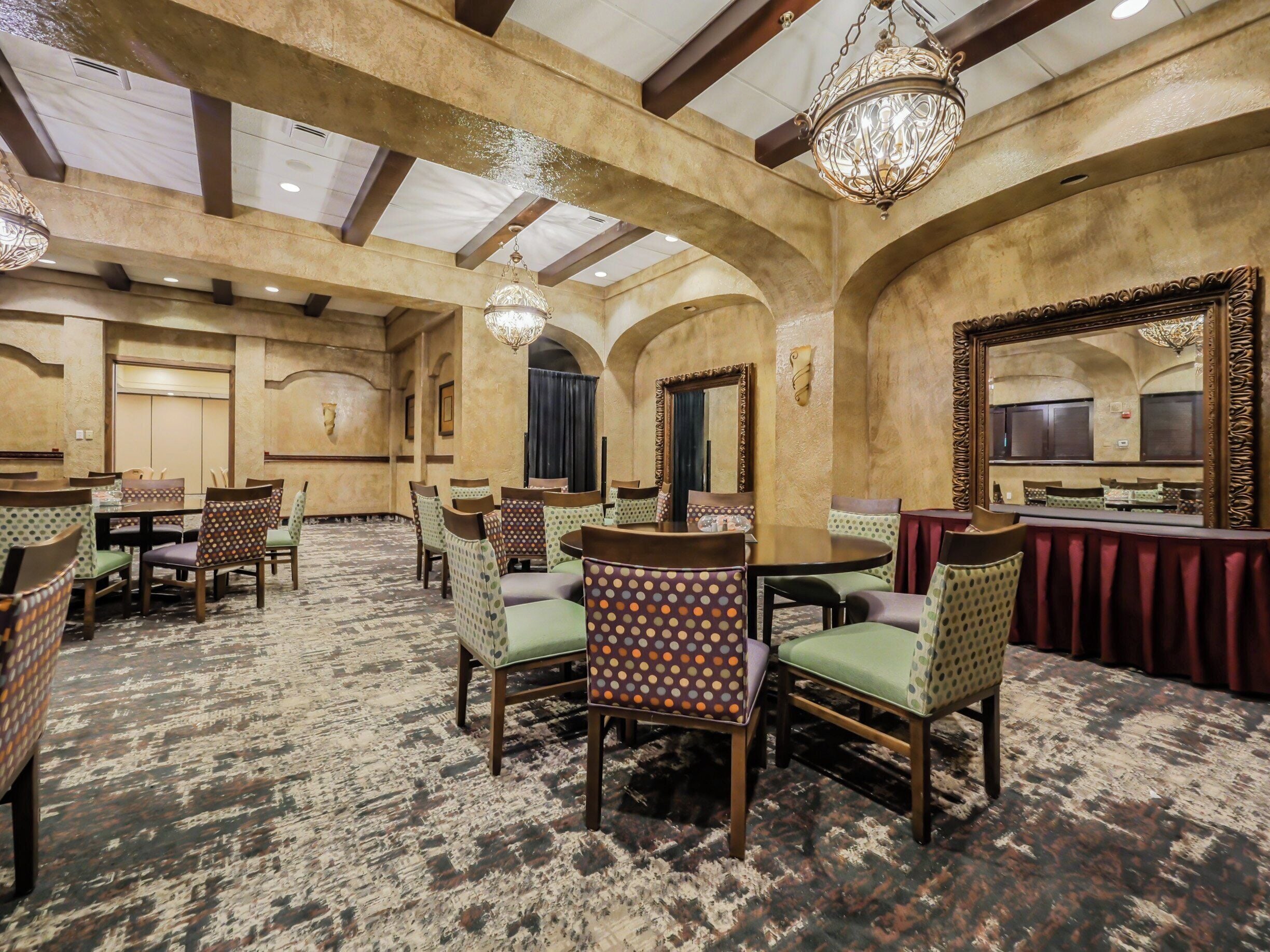A hotel dining area with round tables and chairs, chandeliers, and a patterned carpet.