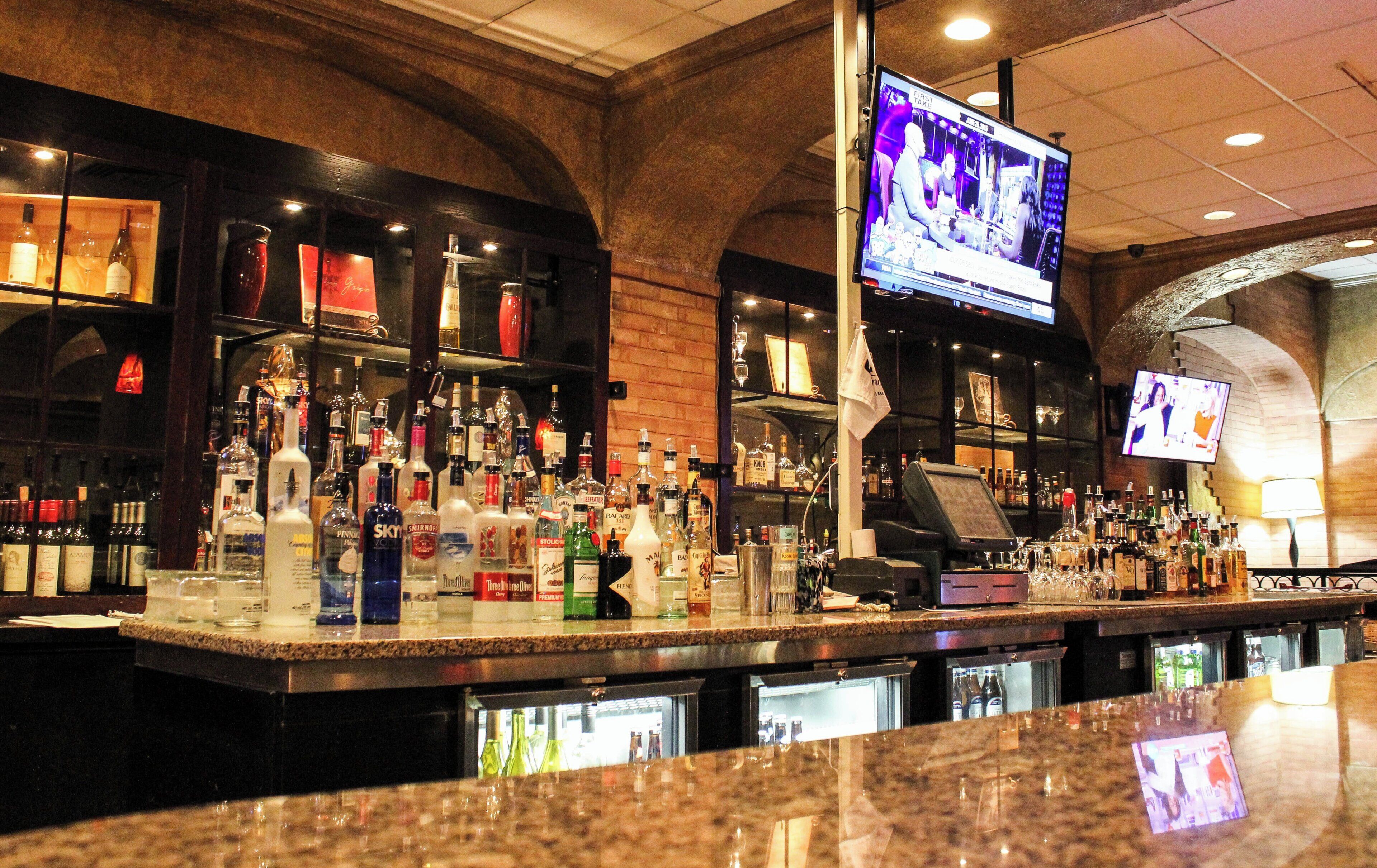 A bar area with a variety of liquor bottles, a television screen, and a cash register.