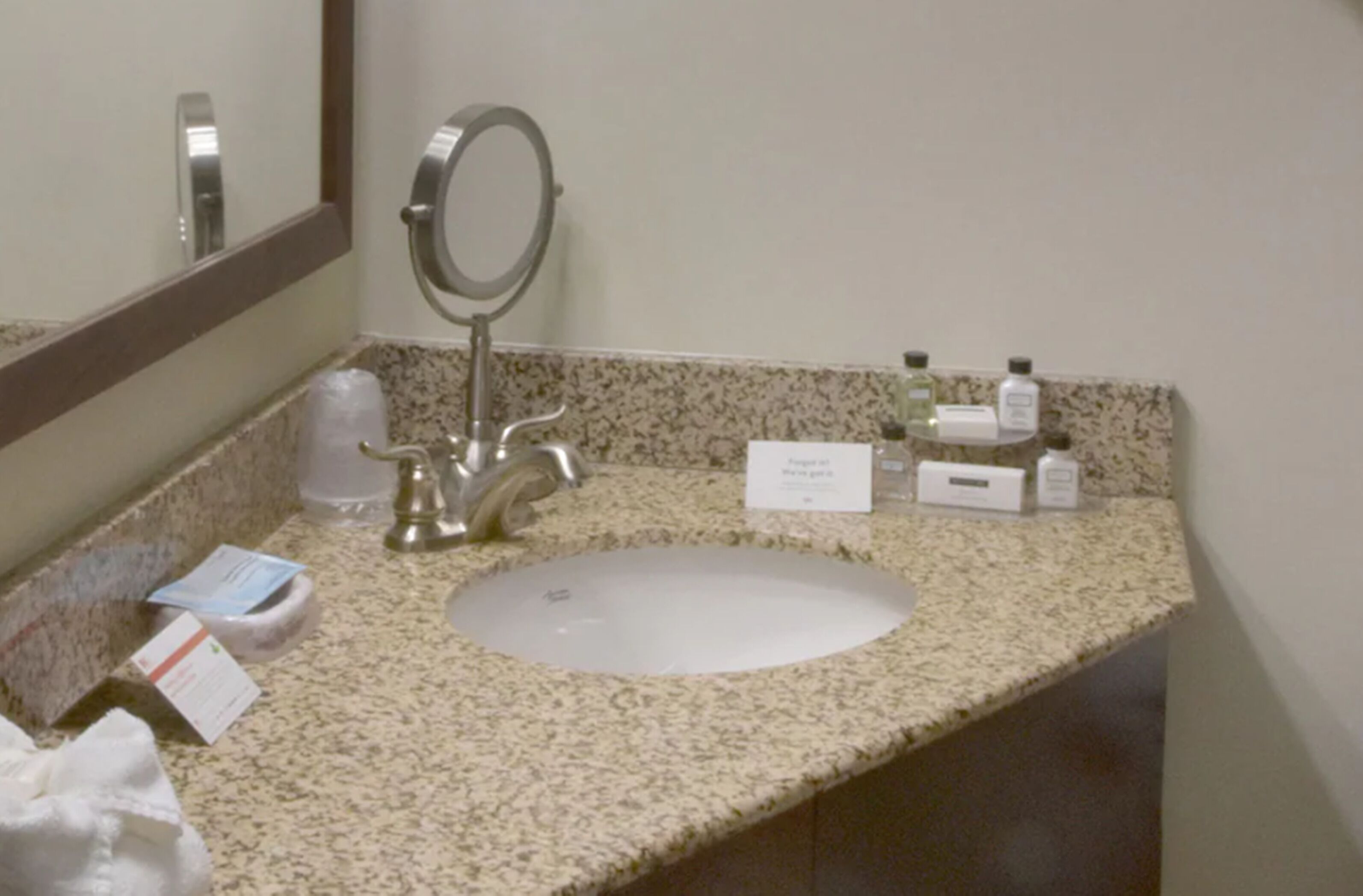 A bathroom with a granite countertop, a sink, a mirror, and toiletries.