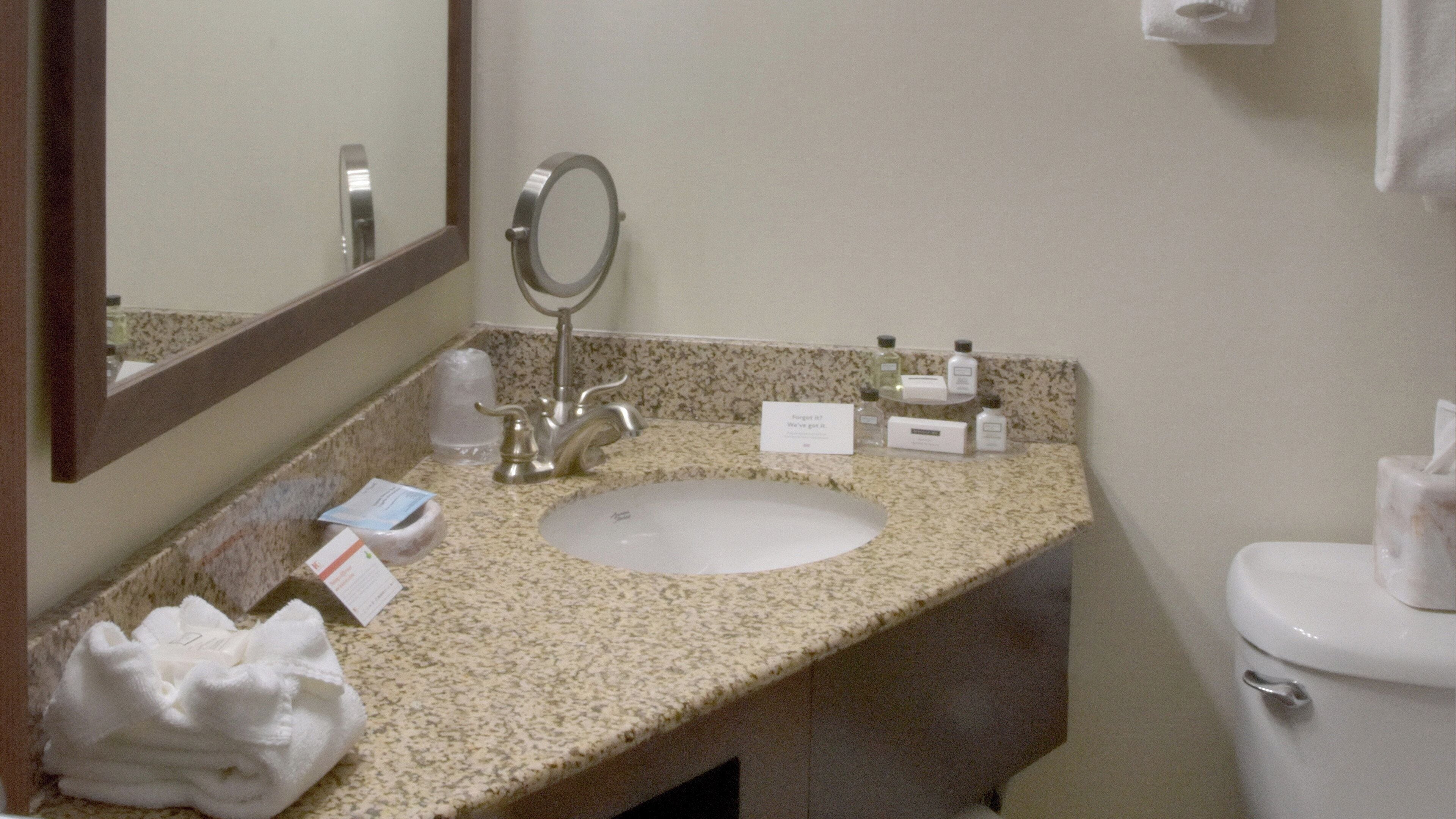 A bathroom with a sink, mirror, toiletries, and a toilet.